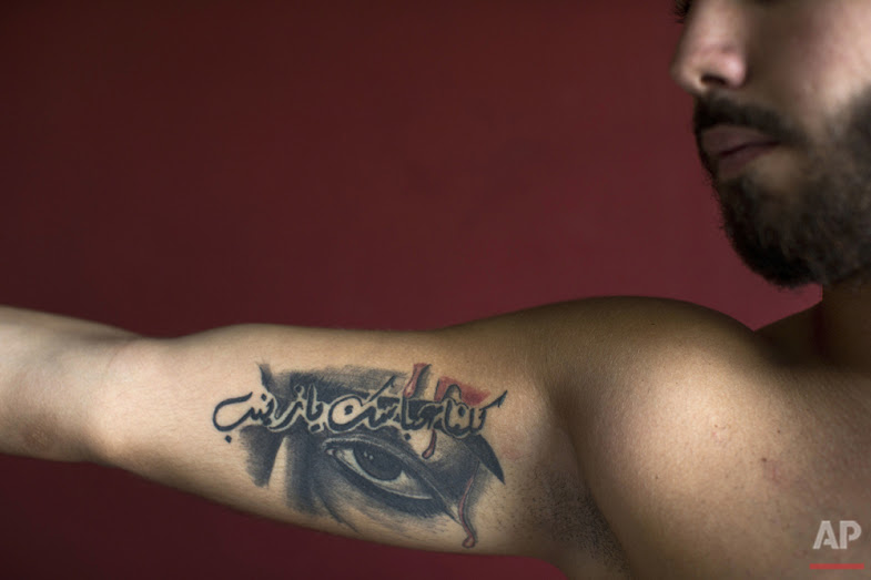 In this Tuesday, May 31, 2016 photo, Abbas, 23, poses for a photo showing off his tattoos of Shiite Muslim religious slogans with Arabic that reads "We are all your Abbas, oh Zeinab," in the southern suburb of Beirut. (AP Photo/Hassan Ammar)