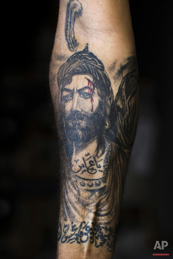 In this Tuesday, May 10, 2016 photo, Ali Hussein Nasreddine, 50, poses for a photo showing off his tattoo of Imam Abbas with blood on his face in the southern suburb of Beirut. The tattoo in Arabic reads, "Oh Abbas." (AP Photo/Hassan Ammar)