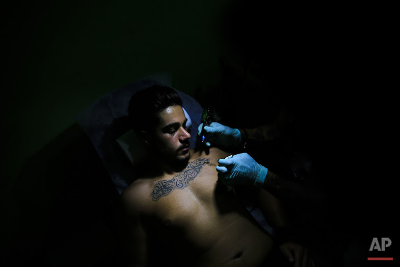 In this Wednesday, July 20, 2016 photo, tattoo artist Hussein Al-Hussein inks the chest of client Alodi Issa, 22, with Shiite Muslim religious slogans at his tattoo shop in the southern suburb of Beirut. The tattoo in Arabic reads, "Oh, the revenge for Hussein. Ali, Fatima." (AP Photo/Hassan Ammar)
