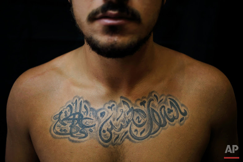 In this Monday, July 18, 2016 photo, Alodi Issa, 22, poses for a photo showing off his tattoos with Shiite Muslim religious slogans in the southern suburb of Beirut. The tattoo in Arabic reads, "Oh, the revenge for Hussein. Ali, Fatima." (AP Photo/Hassan Ammar)